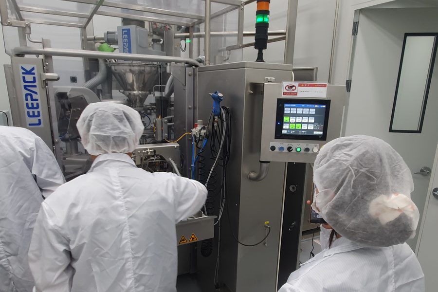 The Lentila team in lab coats and hairnets beside a pouch-filling line.